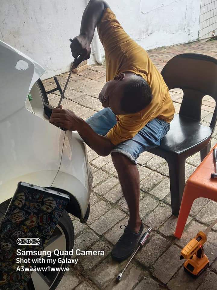 Paintless dent removal technician using PDR rod on white car panel